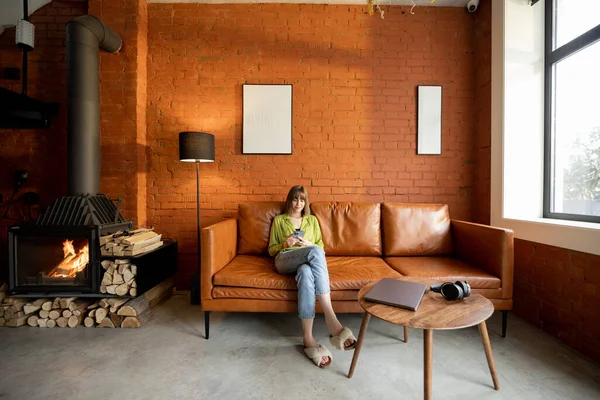 Woman sits with gadgets in modern living room in loft style at home