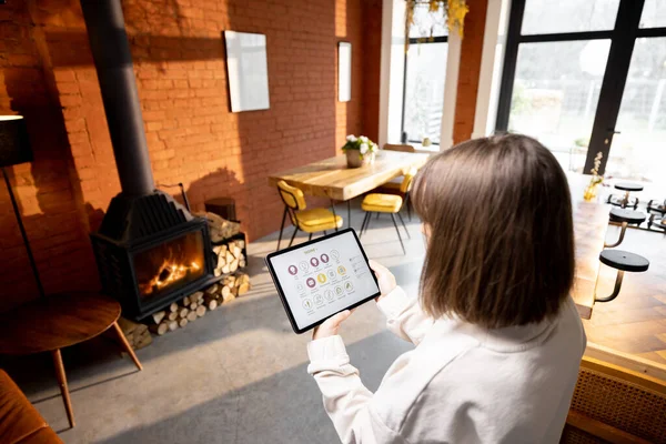 Женщина, управляющая домашними устройствами удаленно, используя умное домашнее приложение на цифровом планшете дома — стоковое фото