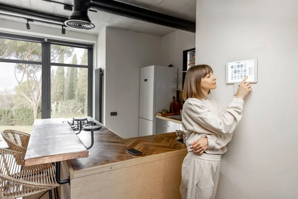 Woman controlling home devices with digital smart panel mounted on the wall