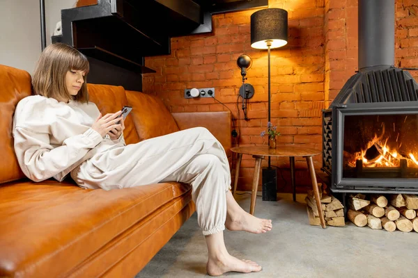 Mujer sentada relajada en un sofá y usando el teléfono en casa —  Fotos de Stock