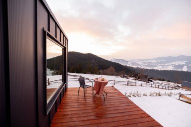 Teraslı küçük bir ev ve dağlarda büyük bir pencere.