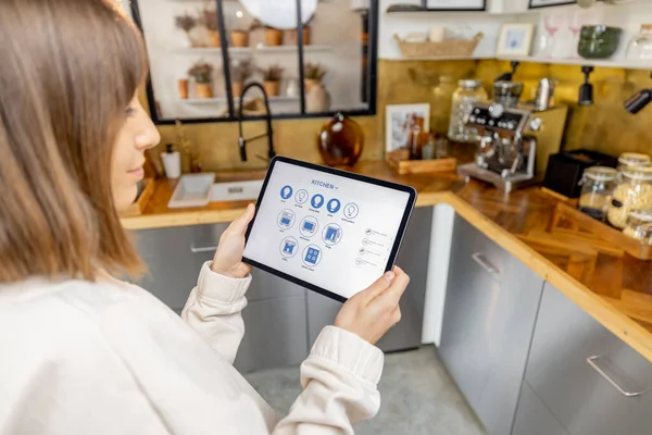Kvinna håller digital tablett med kör smarta hem ansökan i köket — Stockfoto