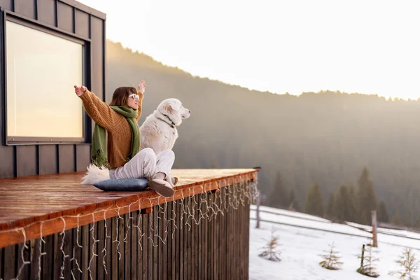 Köpeğiyle birlikte doğadaki küçük evin terasında dinlenen bir kadın. — Stok fotoğraf