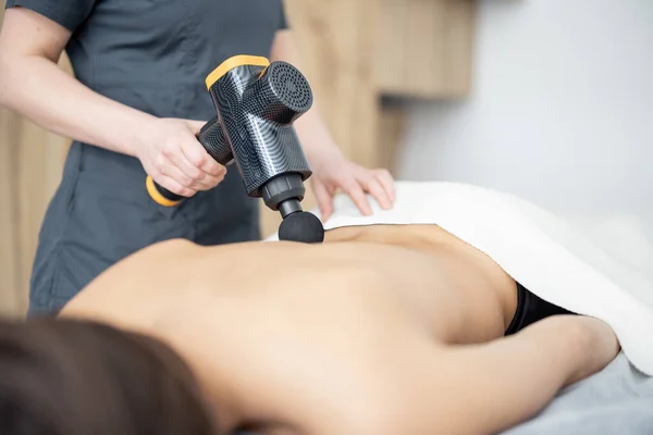 Woman massages the patients back with a percussion massager — Stock Photo, Image