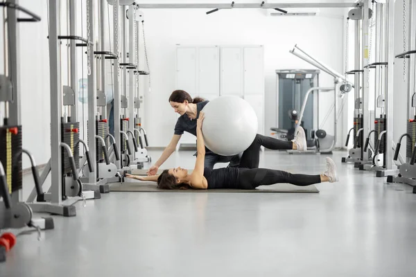 Γυναίκα κάνει ασκήσεις με μπάλα γυμναστικής με ειδικό αποκατάστασης στο γυμναστήριο — Φωτογραφία Αρχείου