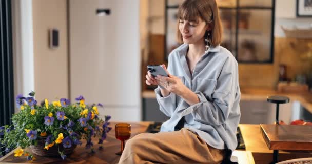 Vrouw zit op een keukenblad met telefoon bij mooi huis — Stockvideo