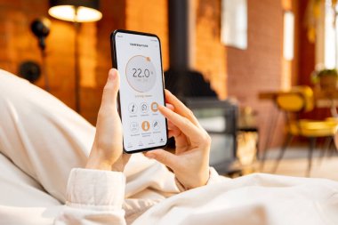 Sıcaklık kontrolü için akıllı ev uygulaması çalıştıran bir kadın telefonu tutuyor