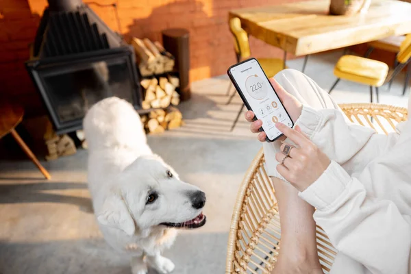 Frau nutzt Smartphone mit Smart-Home-App zu Hause mit Hund — Stockfoto