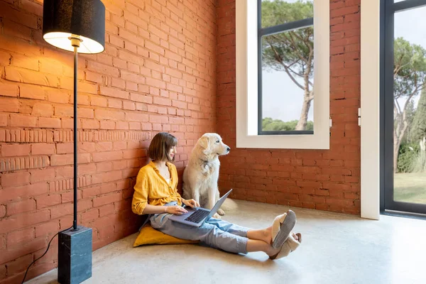 Mujer trabajando en el ordenador portátil mientras está sentada con su perro en casa —  Fotos de Stock