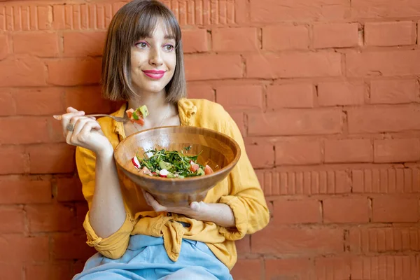 坐在砖墙背景下吃健康沙拉的女人 — 图库照片