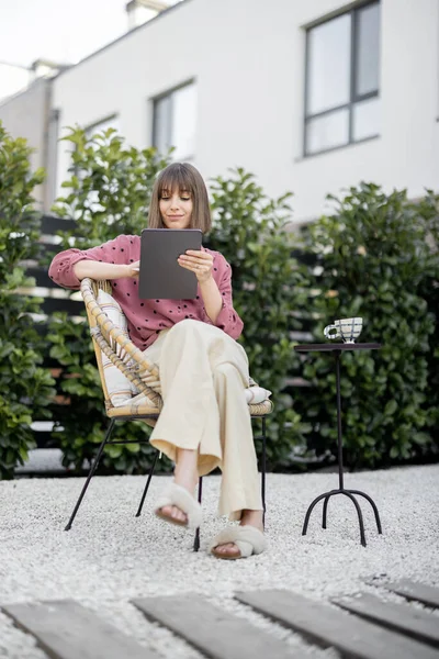 Жінка працює на цифровому планшеті, сидячи розслабленим на задньому дворі — стокове фото