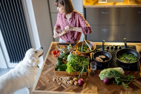 Genç ev hanımı, sevimli beyaz köpeğiyle mutfakta salata yapıyor. — Stok fotoğraf