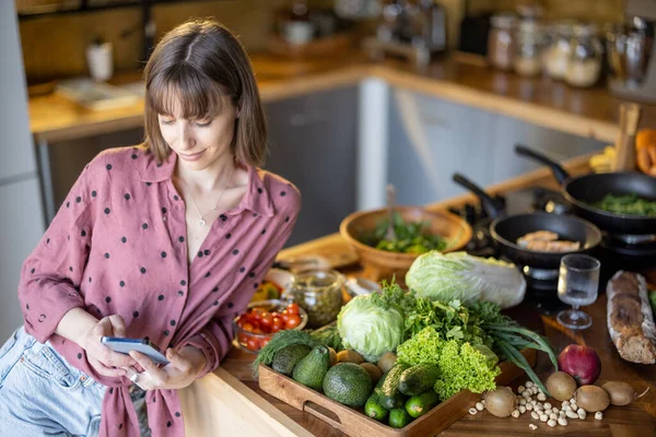Γυναίκα που χρησιμοποιεί smatphone ενώ το μαγείρεμα υγιεινά στο σπίτι — Φωτογραφία Αρχείου