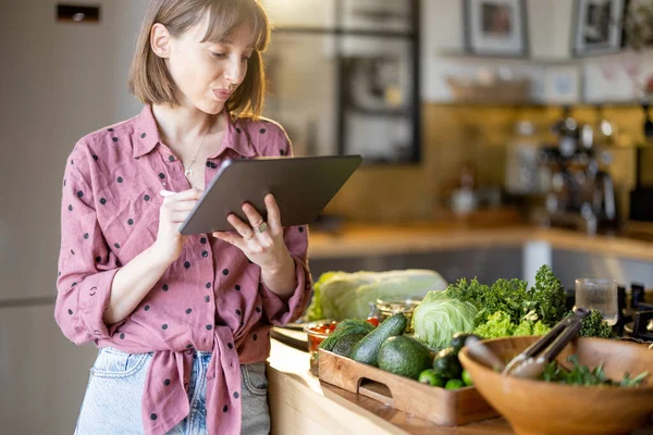 Woman using digital tablet while cooking healthy at home — ストック写真