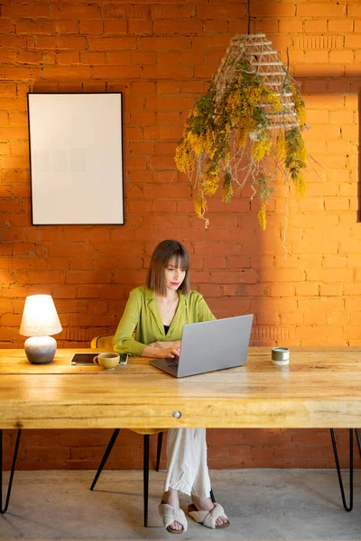 Donna lavora sul computer portatile mentre seduto vicino al tavolo di legno a casa accogliente — Foto Stock