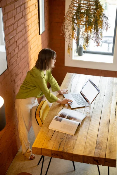 Vrouw werkt op laptop terwijl zittend aan de houten tafel in gezellige woonkamer — Stockfoto