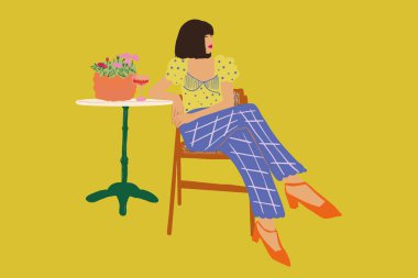 Arka planda çiçekler olan şık bir kadın masada oturuyor.