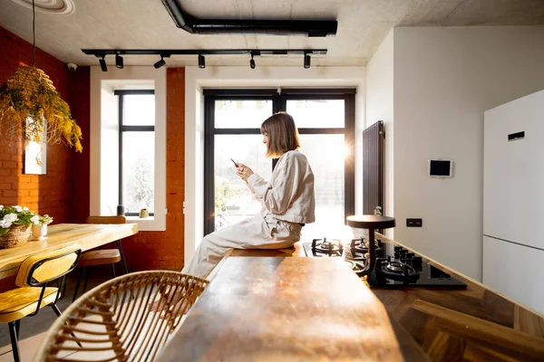Kvinna som använder telefon när du sitter ensam på ett köksbord hemma — Stockfoto
