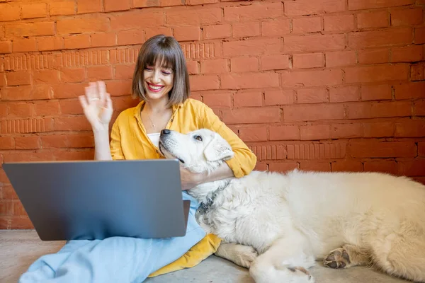 Mujer que tiene videollamada en el ordenador portátil mientras está sentada con su lindo perro blanco — Foto de Stock
