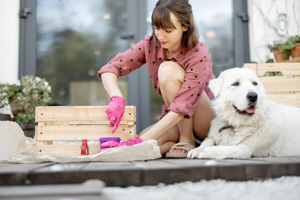 Жінка малює дерев'яну коробку, сидячи з собакою на терасі — стокове фото