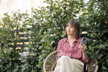 Kadın açık havada akıllı telefon ve dijital tablet üzerinde çalışıyor.
