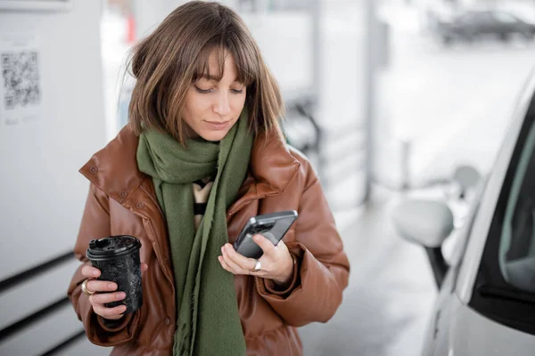 Portrét mladé ženy s telefonem a kávou jít na čerpací stanici venku — Stock fotografie
