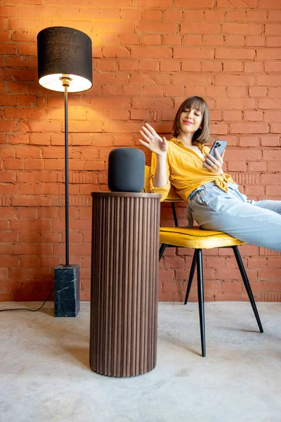 Mujer con altavoz inteligente y teléfono en casa — Foto de Stock