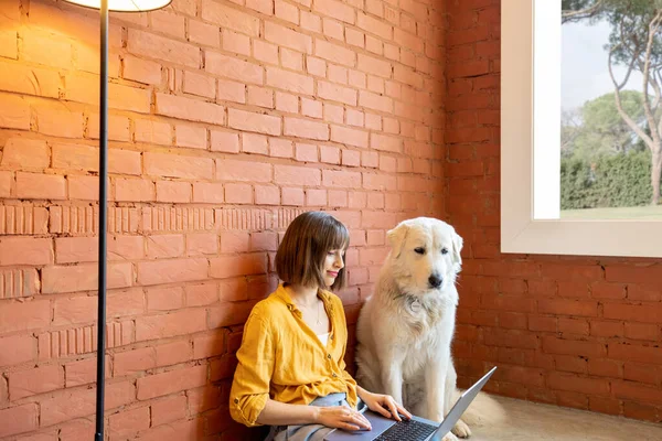 Kvinna som arbetar på bärbar dator medan hon sitter med sin hund hemma — Stockfoto