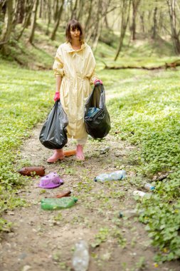 Ormanda dağınık plastik çöpleri toplayan bir kadın.