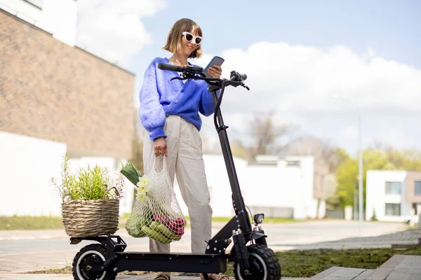 Kadın eve elinde taze sebzelerle elektrikli scooterla gidiyor. — Stok fotoğraf