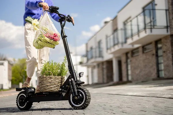 Kadın eve elinde taze sebzelerle elektrikli scooterla gidiyor. — Stok fotoğraf