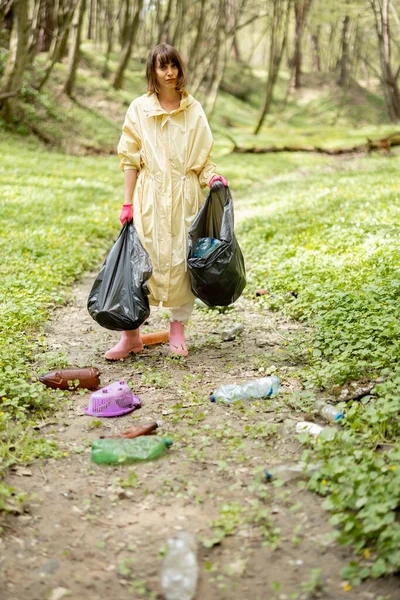 Ormanda dağınık plastik çöpleri toplayan bir kadın.