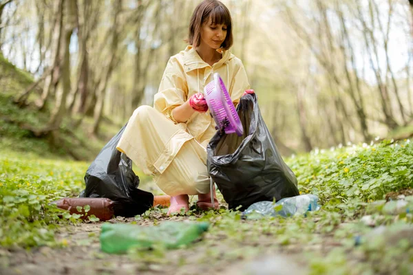 Жінка збирає розкидані пластикові сміття в лісі — стокове фото