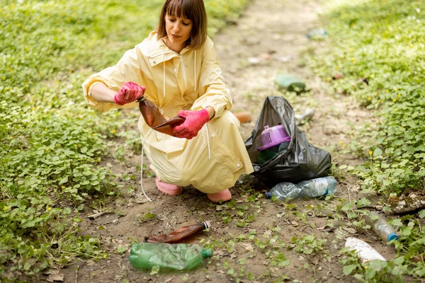 Ormanda dağınık plastik çöpleri toplayan bir kadın.