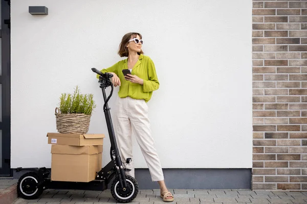 Scooter 'ın yanında elinde paketler ve saksıyla duran bir kadın. — Stok fotoğraf