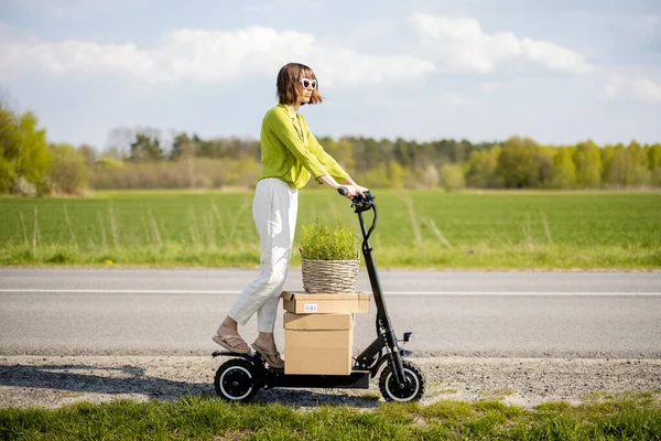 Mulher dirigindo scooter elétrico com parcelas na estrada de campo — Fotografia de Stock