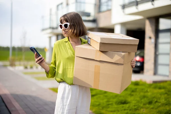 Frau benutzt Handy, während sie mit Paketen auf der Straße steht — Stockfoto