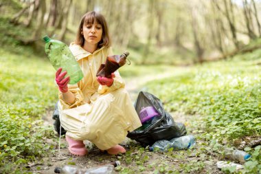 Ormanda dağınık plastik çöpleri toplayan bir kadın.