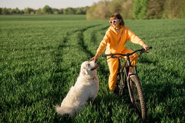 Woman rides a bicycle on a field with her dog — Stock fotografie