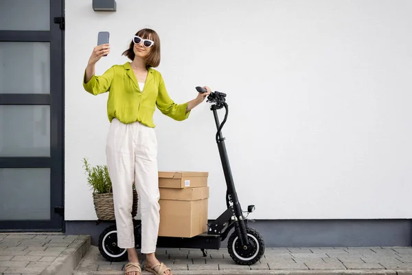 Woman talking on phone while standing with scooter near home — Stock fotografie
