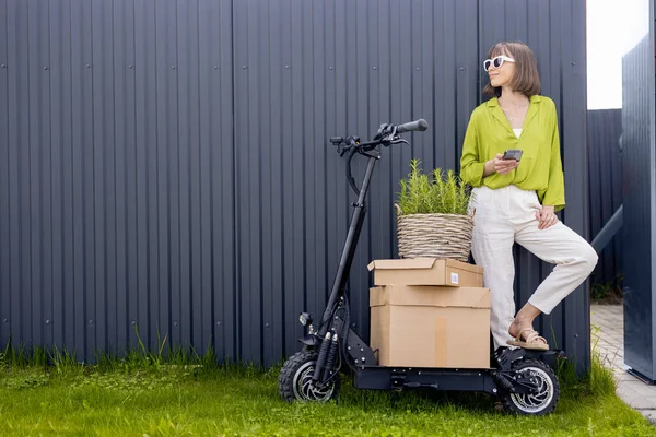 Woman delivering goods by electric scooter — Stockfoto