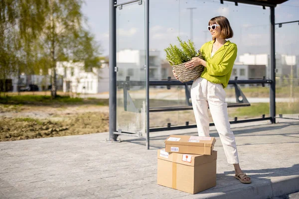 Frau mit Paketen und Blumentopf an Bushaltestelle — Stockfoto