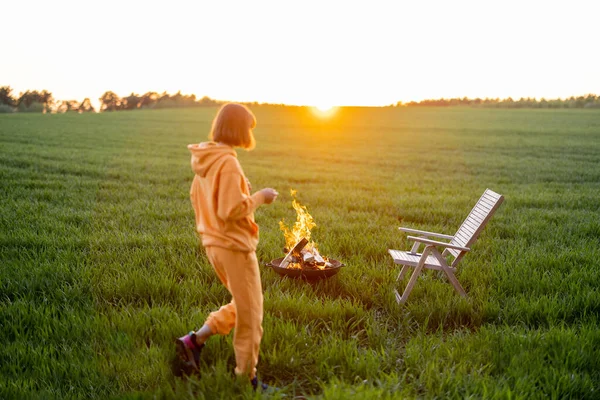 Woman relaxing by the fireplace on green field on sunset — стоковое фото