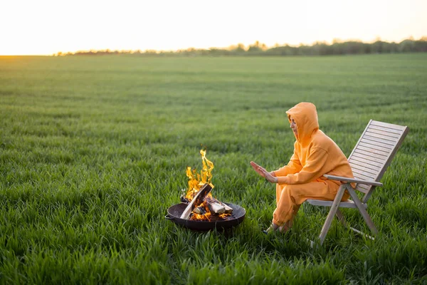 Young person sitting by the fireplace on green field on sunset — Stock Photo, Image