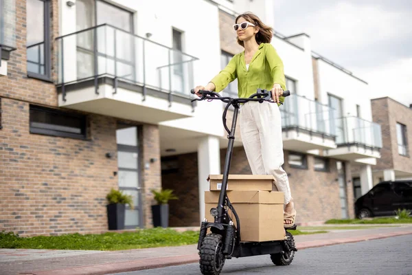 Woman driving electric scooter with cardboard packages — Zdjęcie stockowe