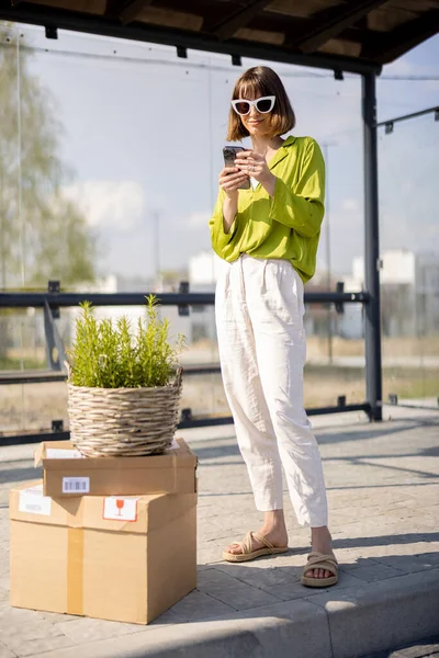 Woman with parcels and flowerpot on a bus stop — Foto de Stock