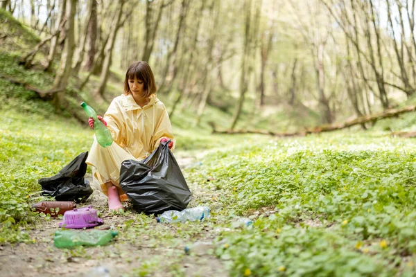 Ormanda dağınık plastik çöpleri toplayan bir kadın.