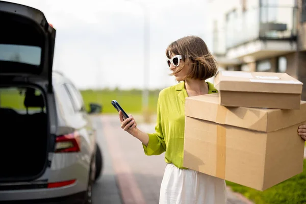 Frau benutzt Handy, während sie mit Paketen auf der Straße steht — Stockfoto