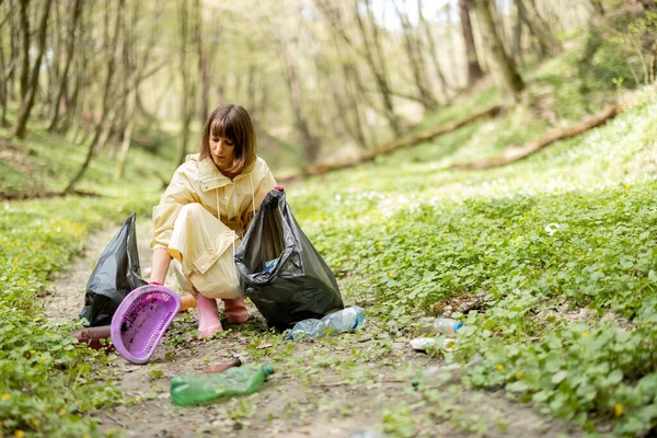 Ormanda dağınık plastik çöpleri toplayan bir kadın.