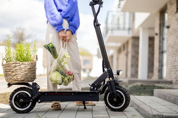 Woman drives on electrical scooter with mesh bag full of vegetables, close-up — стоковое фото